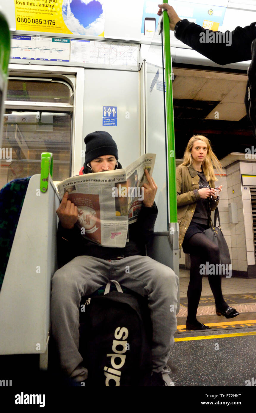 Londres, Angleterre, Royaume-Uni. Homme lisant un journal sur un train de tube (en siège prioritaire) Banque D'Images
