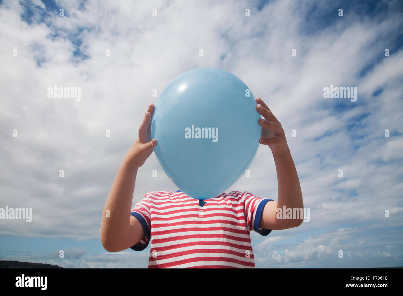 Un garçon debout tenant un ballon en face de son visage. Banque D'Images