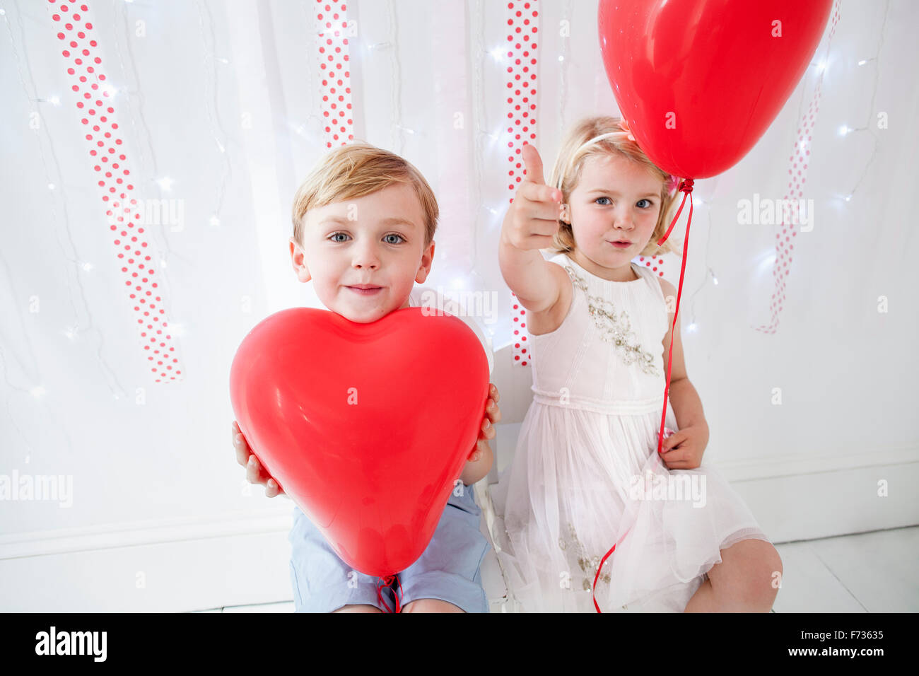 Jeune garçon et fille posant pour une photo dans un studio de photographes, holding red balloons. Banque D'Images