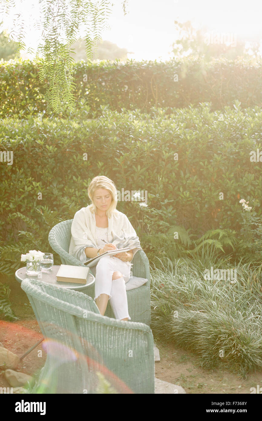 Femme blonde assise dans un fauteuil en osier dans un jardin. Banque D'Images Femme blonde assise dans un fauteuil en osier dans un jardin. Banque D'Images