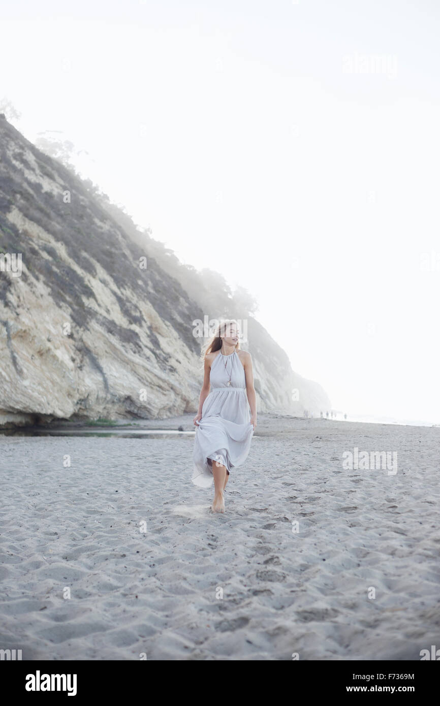 Blonde femme marche sur une plage de sable à proximité d'une falaise. Banque D'Images