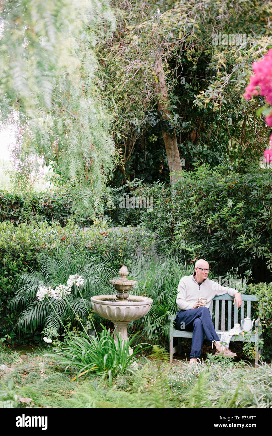 Homme assis sur un banc en bois dans un jardin, de prendre une pause. Banque D'Images