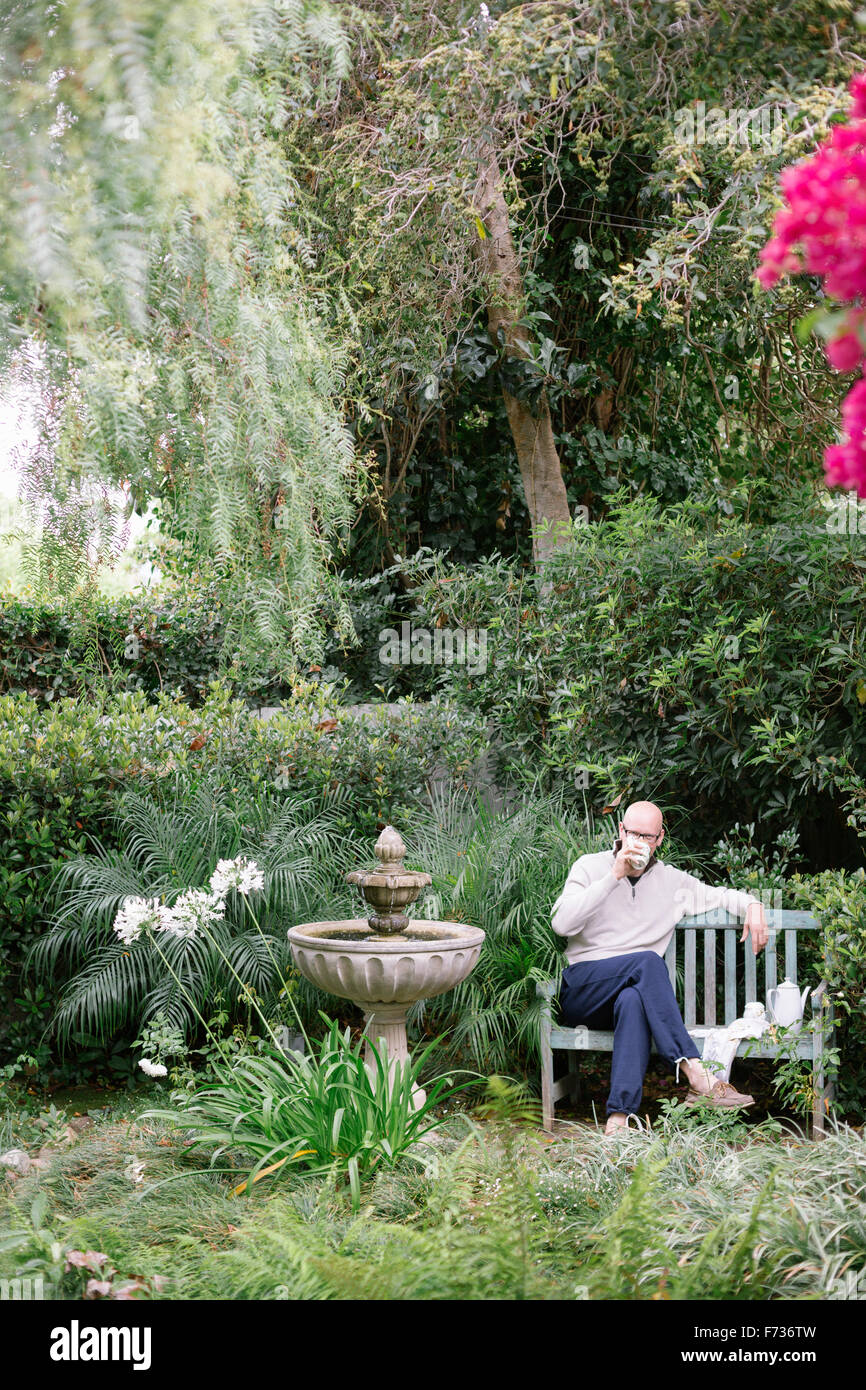 Homme assis sur un banc en bois dans un jardin, de prendre une pause. Banque D'Images