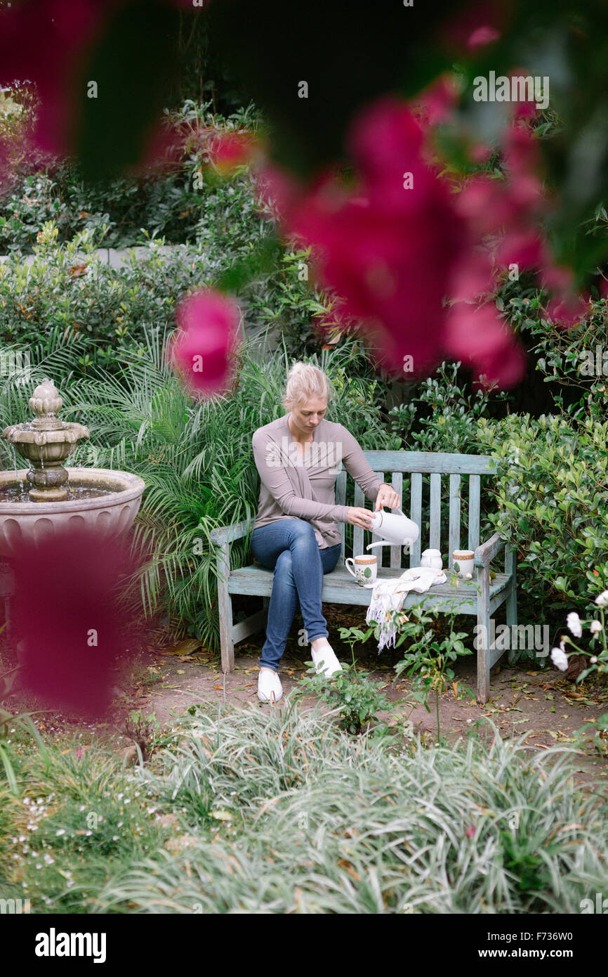 Femme assise sur un banc en bois dans un jardin, de prendre une pause. Banque D'Images