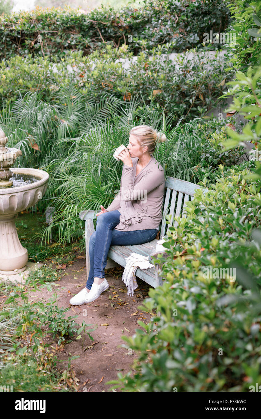 Femme assise sur un banc en bois dans un jardin, de prendre une pause. Banque D'Images