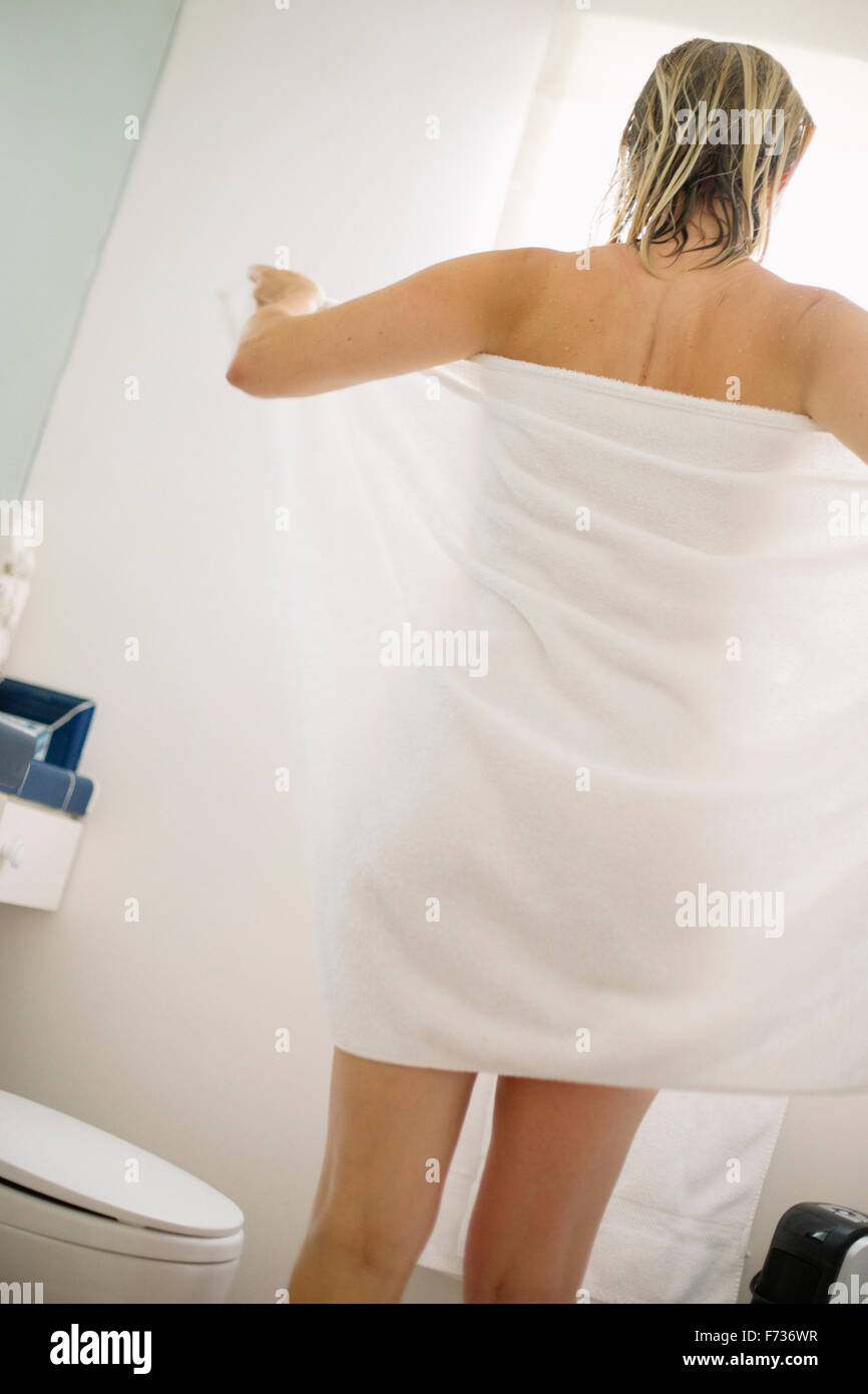 Femme debout dans une salle de bains, enveloppement dans une serviette blanche. Banque D'Images