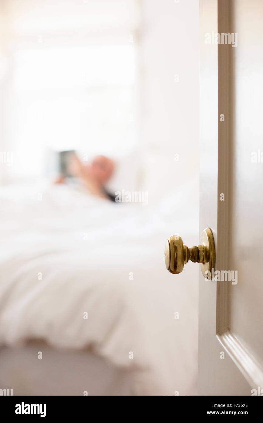 L'homme couché dans un lit avec des draps blancs, lecture. Banque D'Images