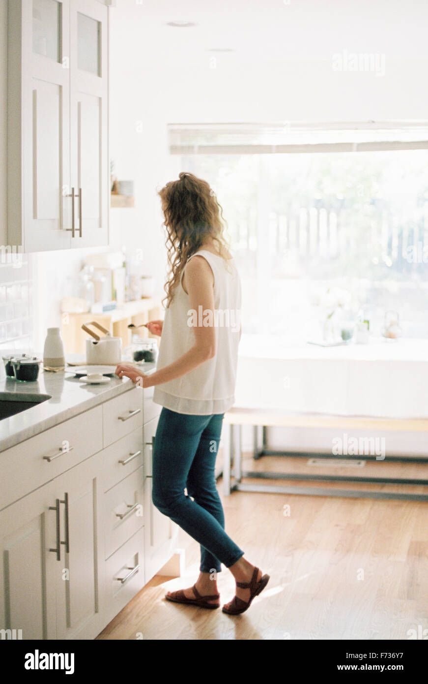 Femme debout dans une cuisine en train de préparer un pot de thé. Banque D'Images