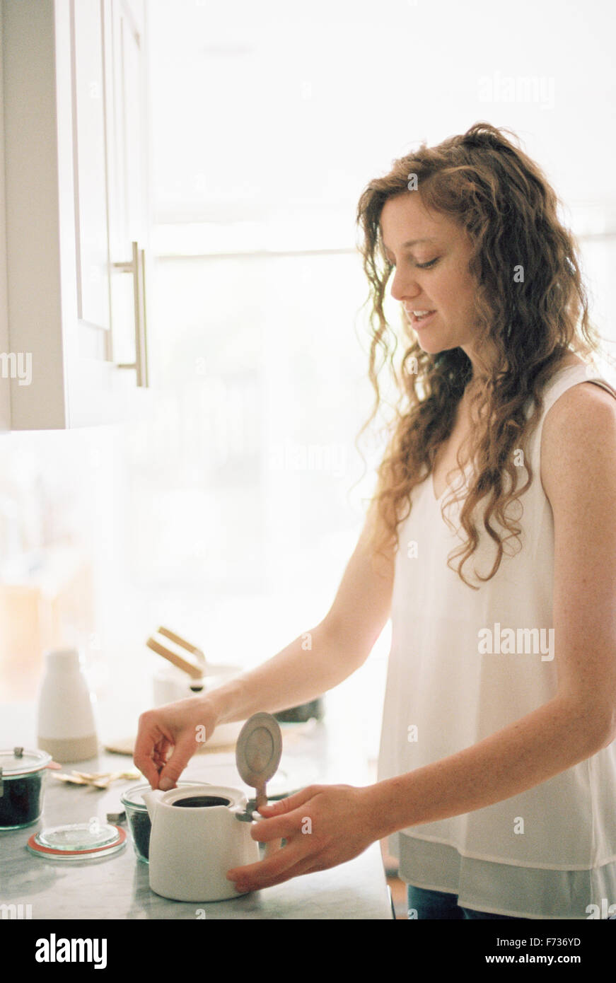 Femme debout dans une cuisine en train de préparer un pot de thé. Banque D'Images