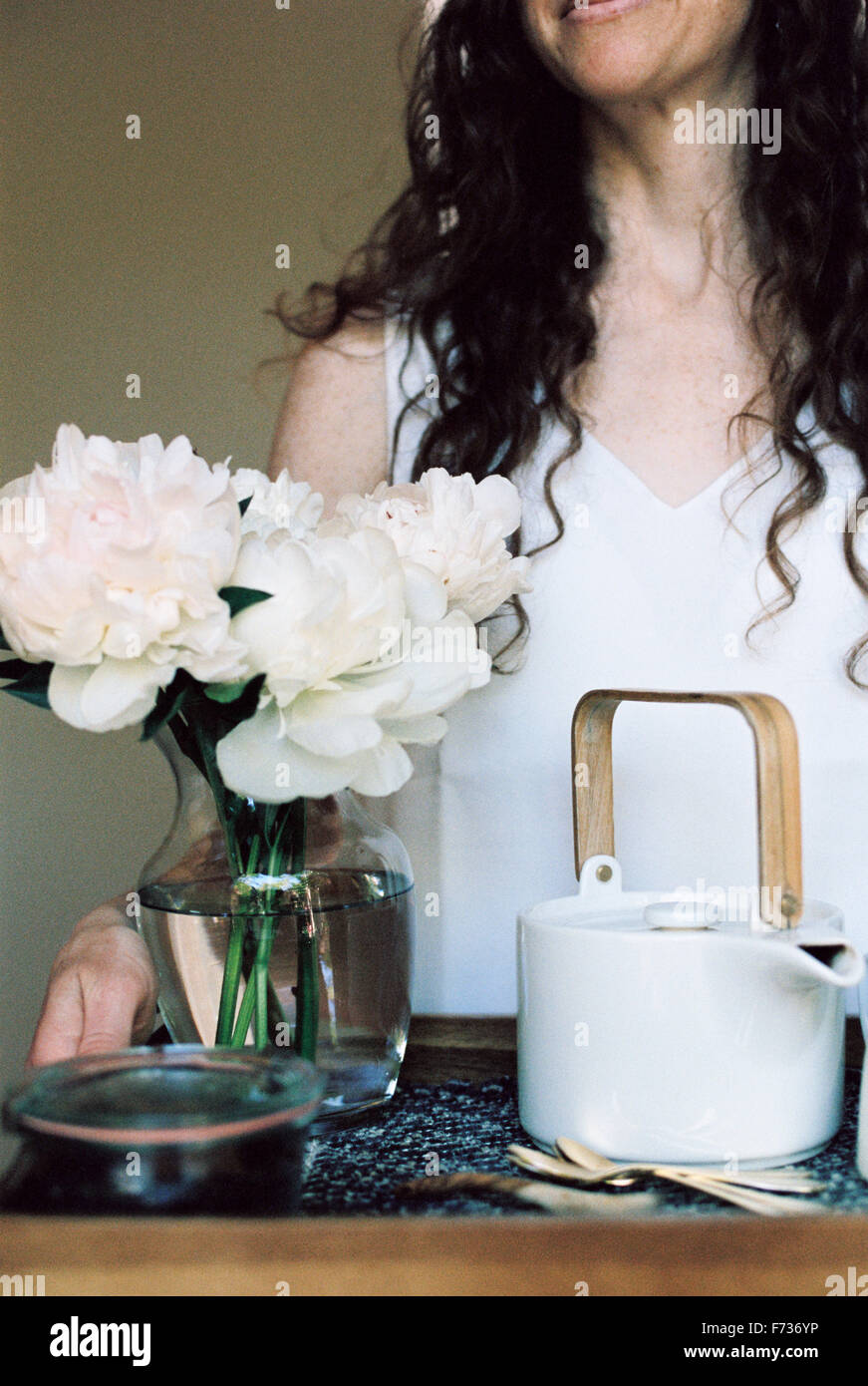 Femme portant un plateau avec une théière et d'un vase de roses blanches. Banque D'Images