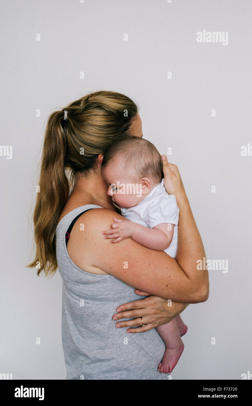 Une femme berçant un enfant, tenant un bébé fille à son épaule. Banque D'Images