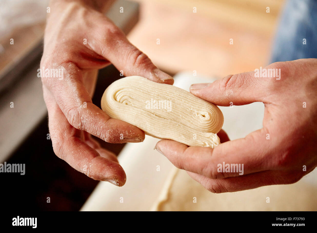 Un baker holding pâte qui a été plié et travaillé pour montrer les couches incorporées dans la pâte, pour préparer des pâtisseries en couches de lumière. Banque D'Images