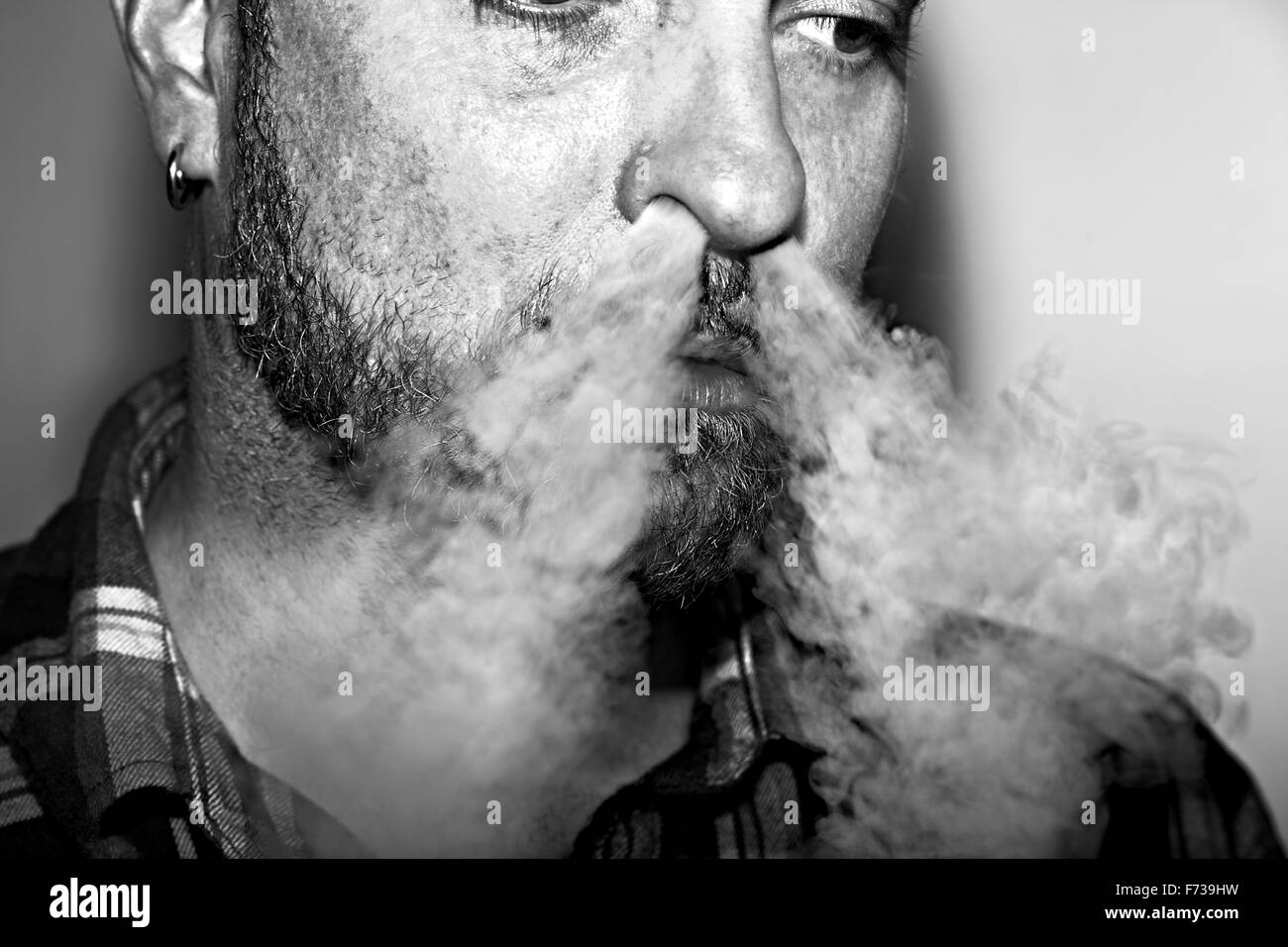 Man blowing vapeur provenant d'un e-cigarette dans ses narines. Banque D'Images