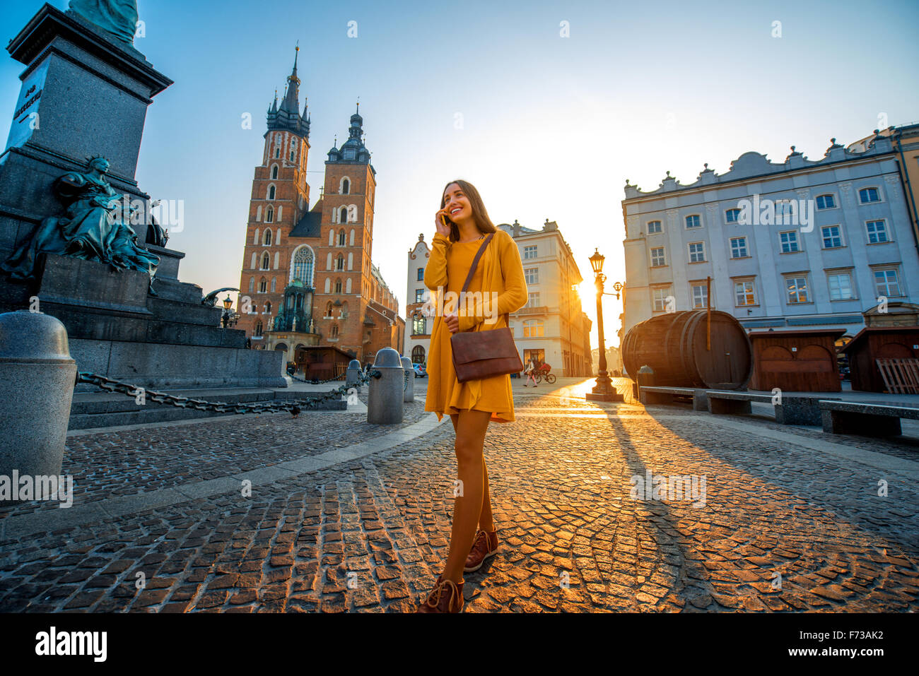 Jeune et belle femme en robe jaune, marchant et parlant avec un téléphone mobile dans le vieux centre-ville de Cracovie le matin Banque D'Images