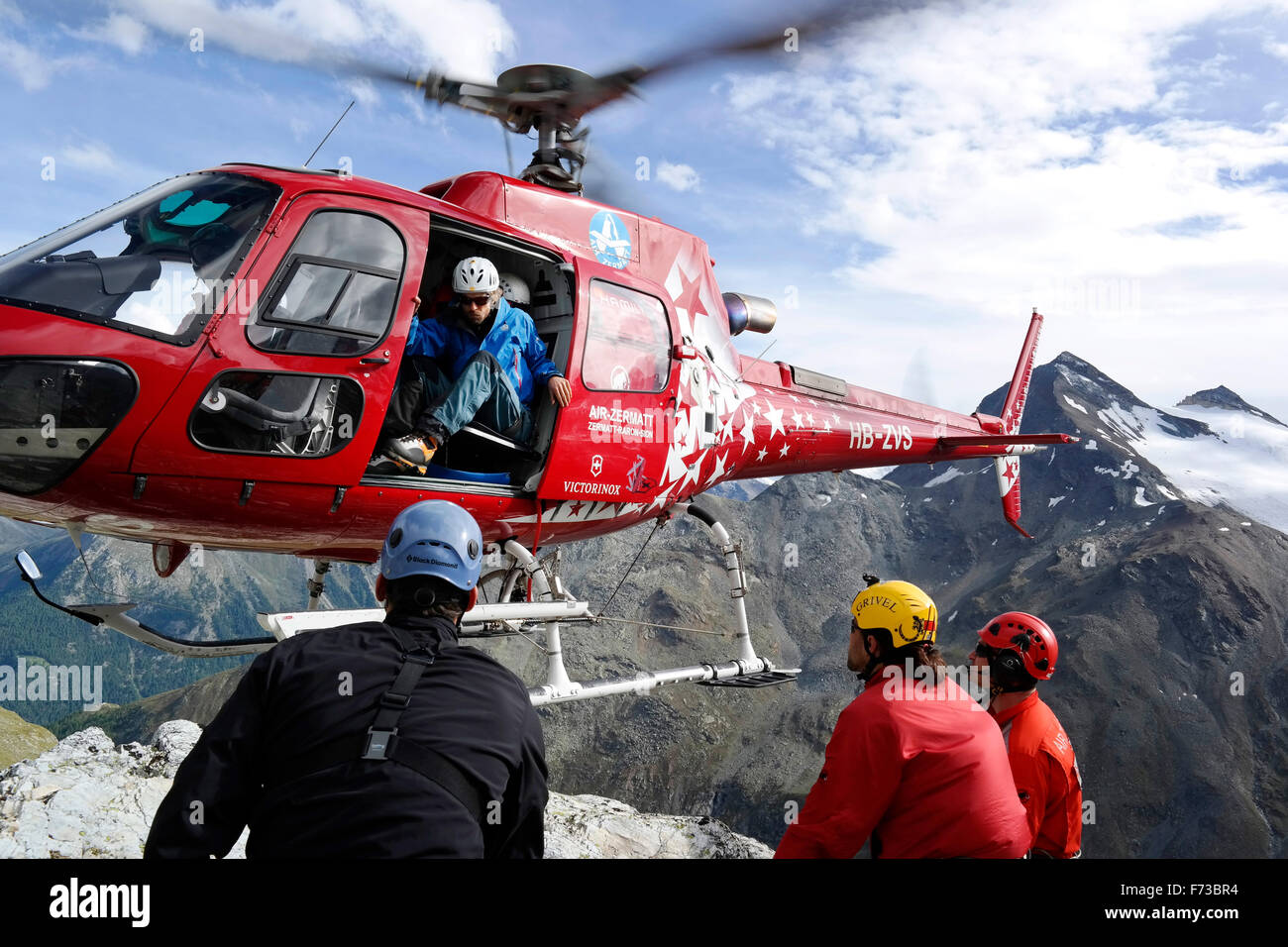 Les secouristes sont à la montagne avec l'atterrissage d'un hélicoptère d'Air Zermatt dans les Alpes suisses. Comme les pales de rotor sont très près du sol, cette sortie en vol stationnaire est une manœuvre délicate. Banque D'Images