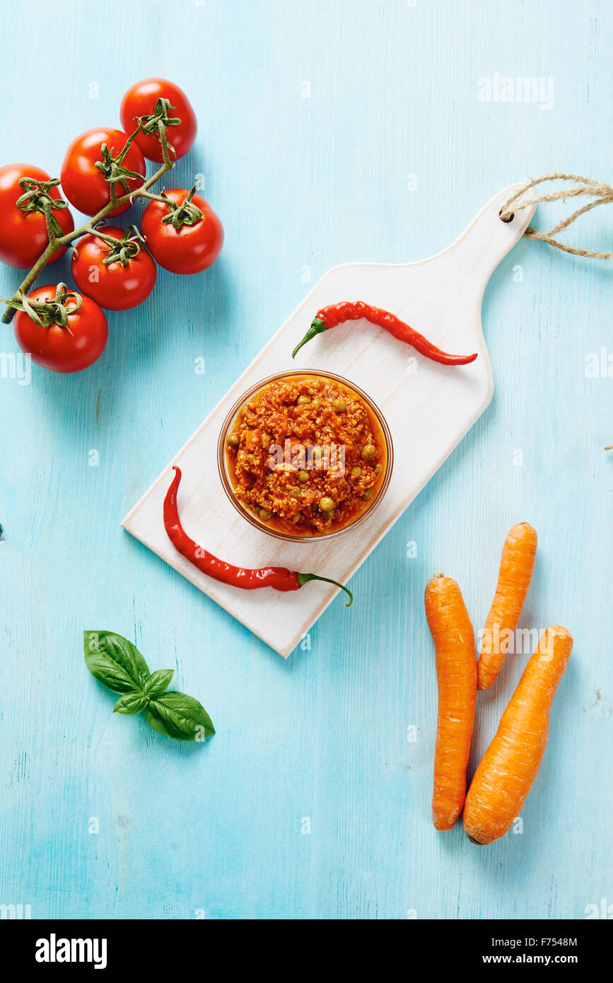 Sauce bolognaise dans bol en verre sur une planche à découper et tableau bleu entouré par des ingrédients Banque D'Images