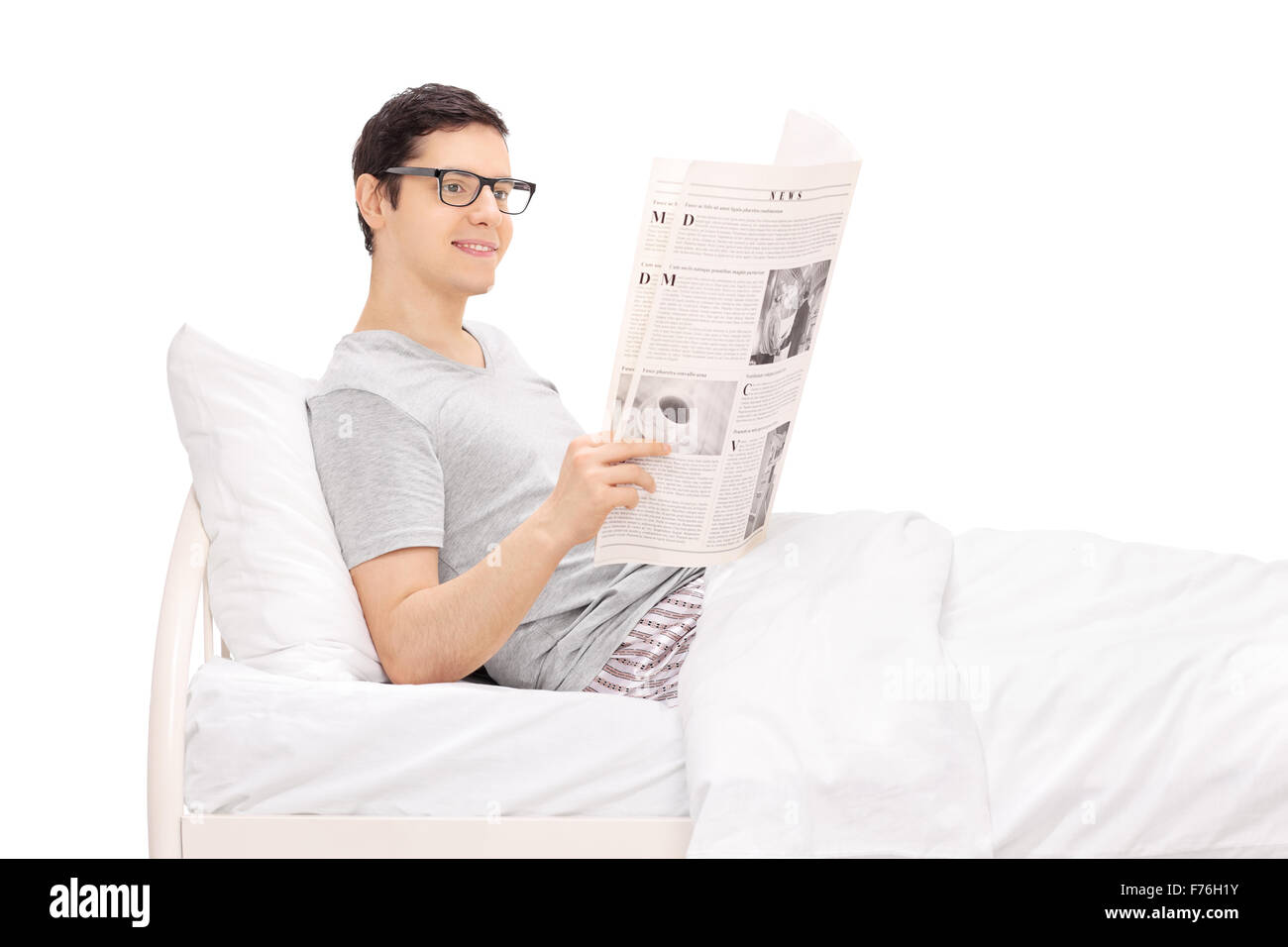 Portrait d'un jeune homme couché dans un lit et lire un journal isolé sur fond blanc Banque D'Images