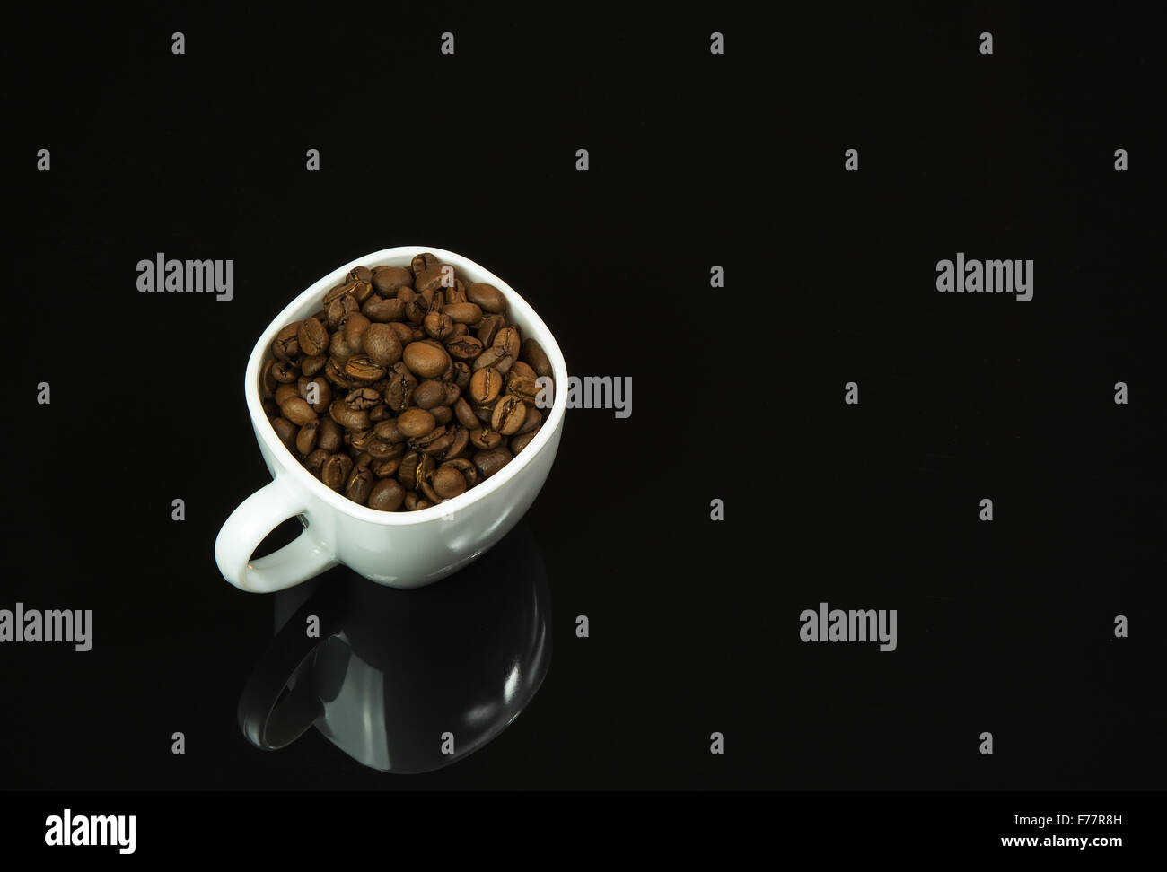 Tasse blanche remplie de grains de café sur un fond noir avec une forte image miroir.vue horizontale. Banque D'Images
