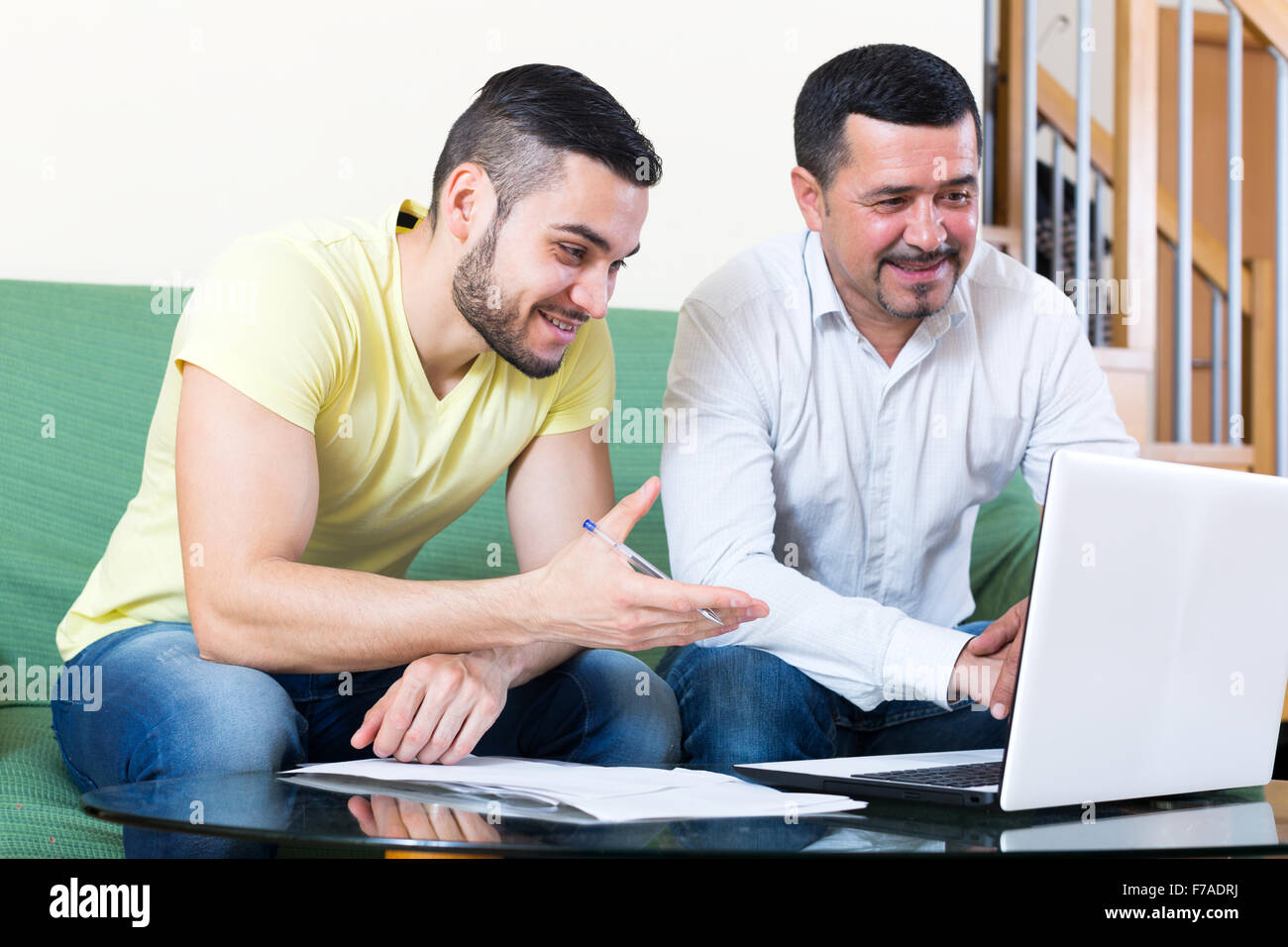 Deux hommes souriant assis à la table et à l'intermédiaire de l'ordinateur portable. L'accent sur l'homme de gauche Banque D'Images