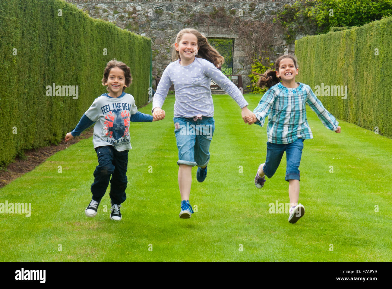 Trois enfants courir le long de l'herbe à la Roseraie à Drum Castle dans l'Aberdeenshire, en Écosse. Banque D'Images