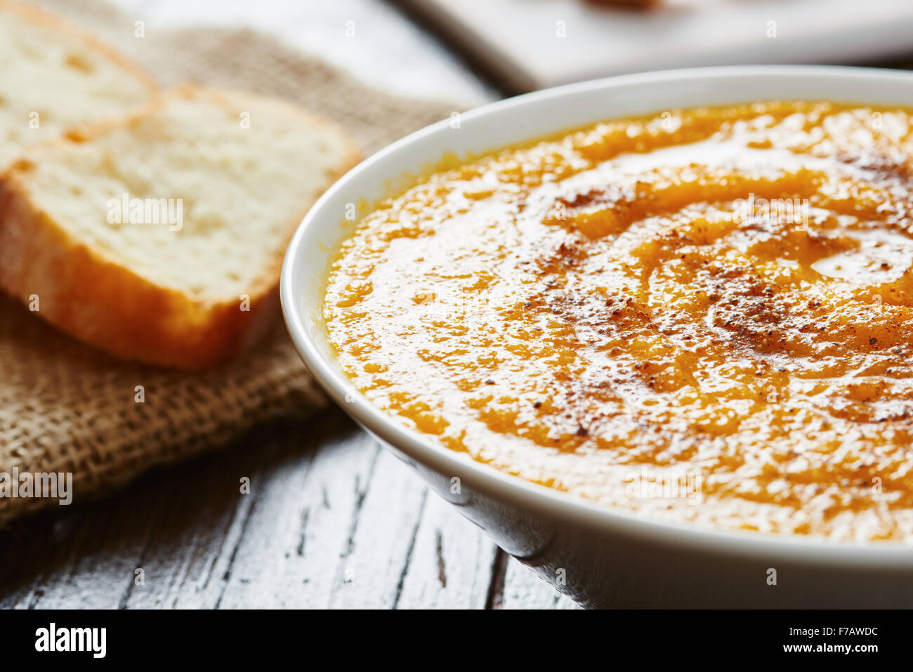 Close-up de la soupe de potiron dans bol blanc avec du pain sur la table en bois croûton Banque D'Images