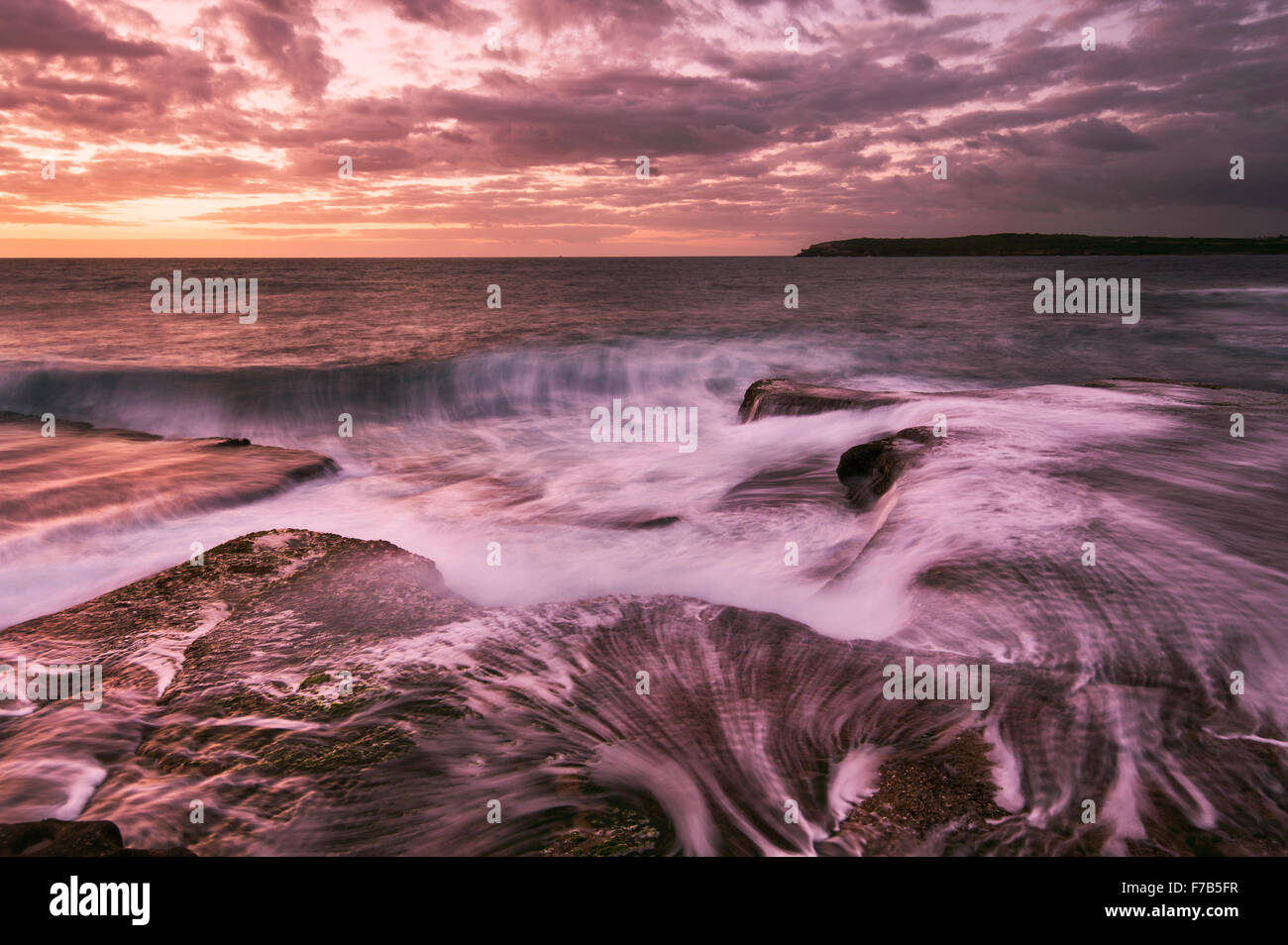 Lever du soleil l'eau avec des vagues et seascape petits rochers cascade dans les tons magenta à Sydney Australie Banque D'Images