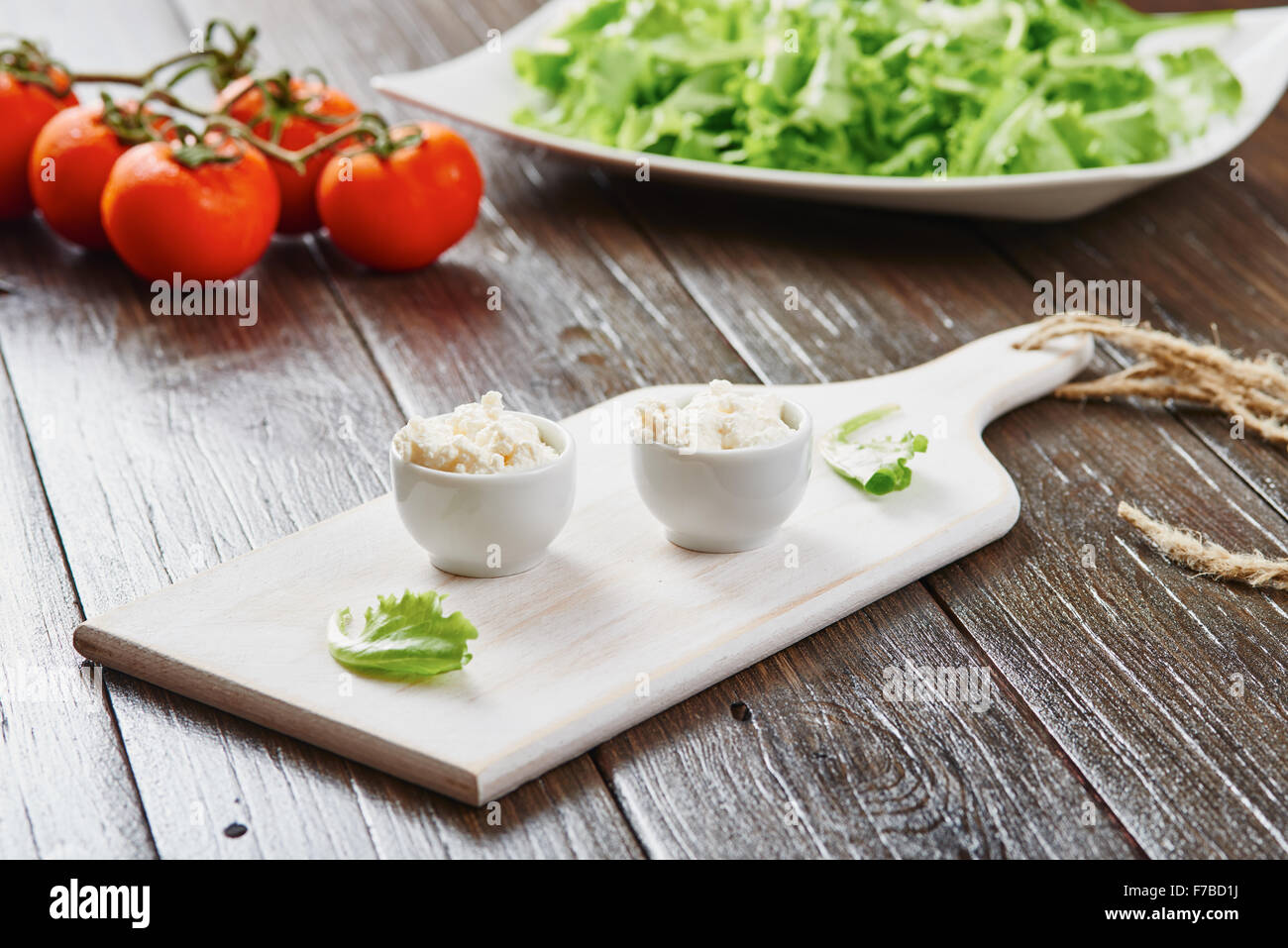 Le fromage cottage dans deux bols sur la table en bois blanc, tomates et salade Banque D'Images
