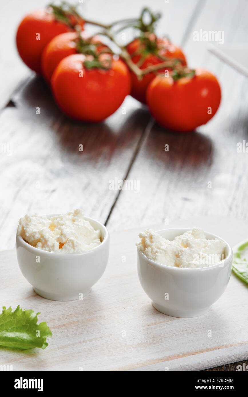 Le fromage cottage dans deux bols sur la table en bois blanc, tomates et salade Banque D'Images