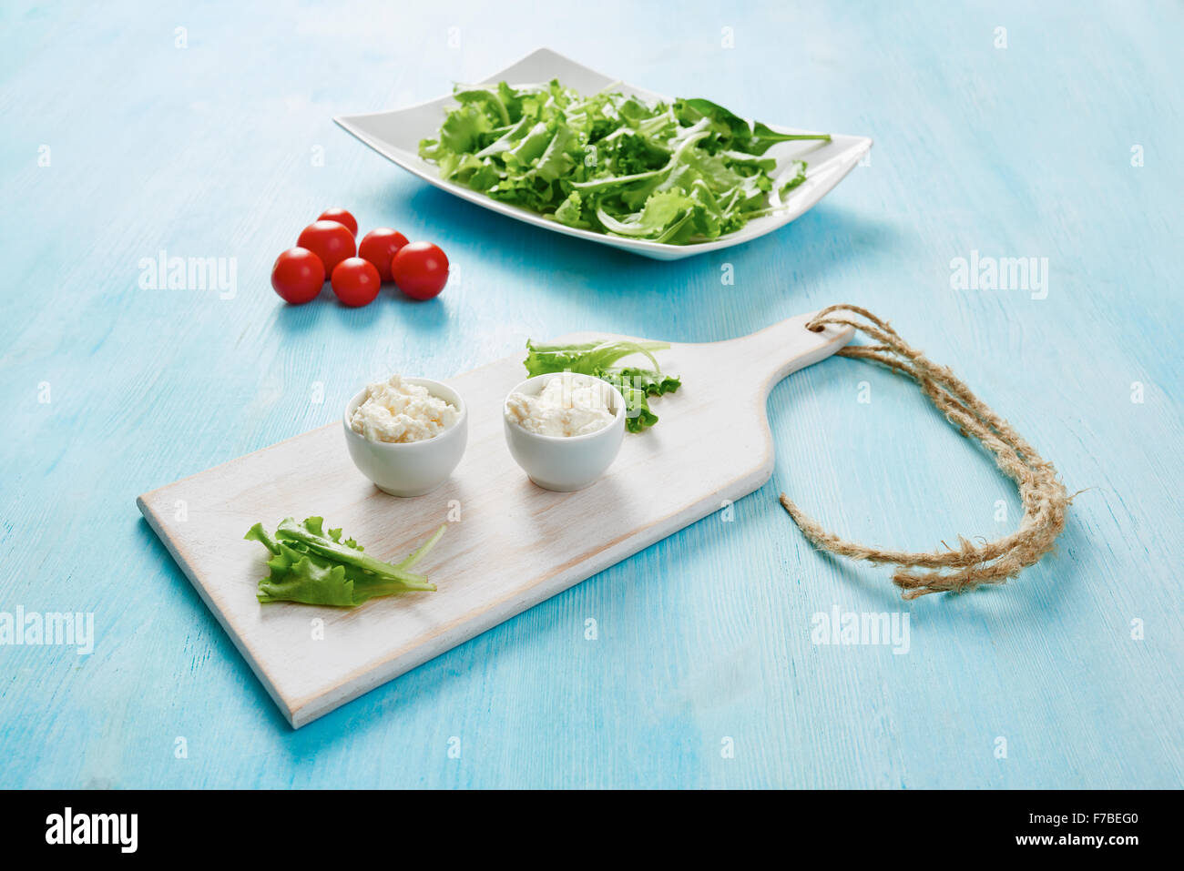 Le fromage cottage dans deux bols blanc sur bleu table en bois, salade et tomate Banque D'Images