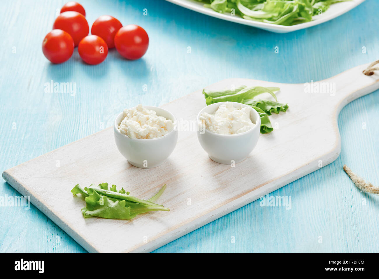 Le fromage cottage dans deux bols blanc sur bleu table en bois, salade et tomate Banque D'Images