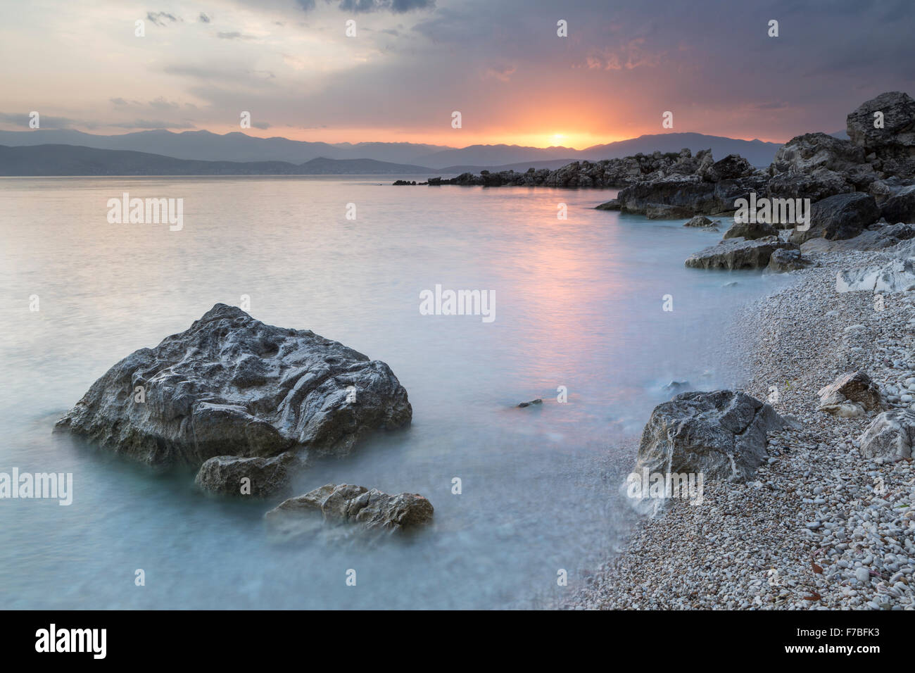 Les cailloux et les rochers sur la plage de Bataria, Kassiopi, Corfou sont éclairés avec la forte lumière orange de lever du soleil. Banque D'Images