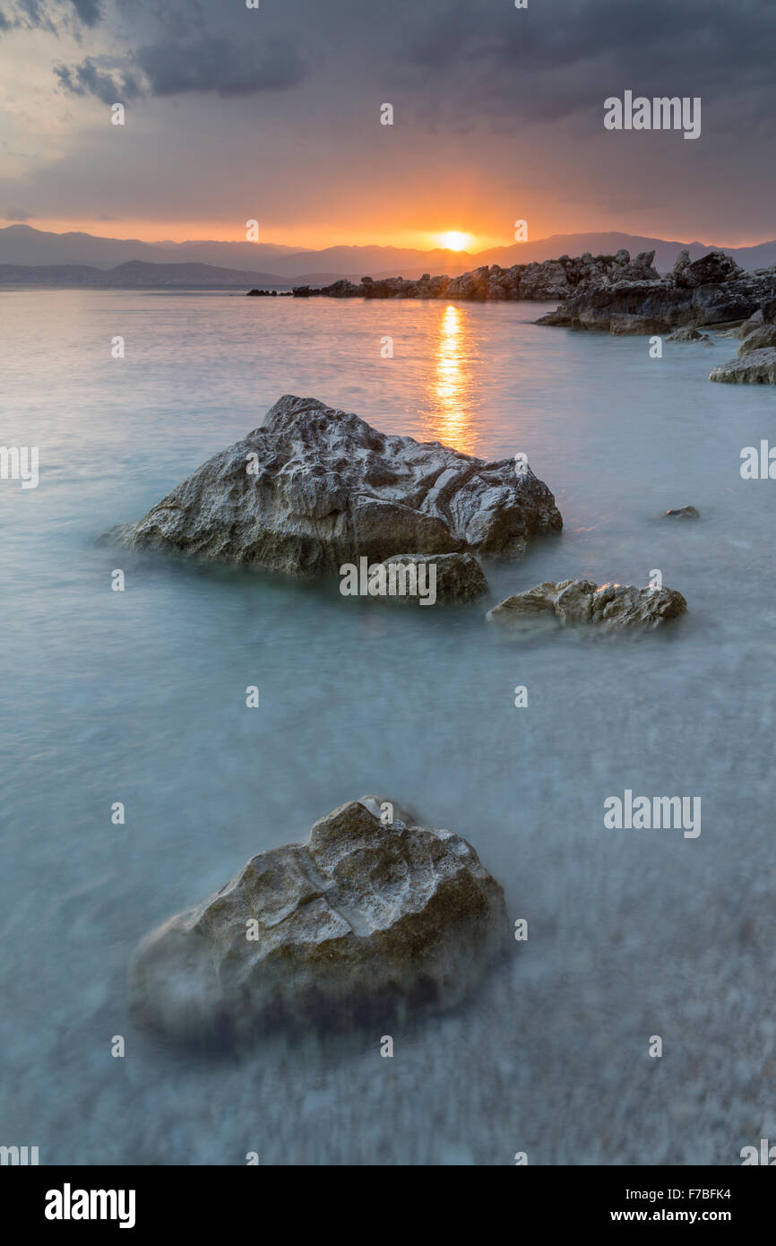 Les cailloux et les rochers sur la plage de Bataria, Kassiopi, Corfou sont éclairés avec la forte lumière orange de lever du soleil. Banque D'Images