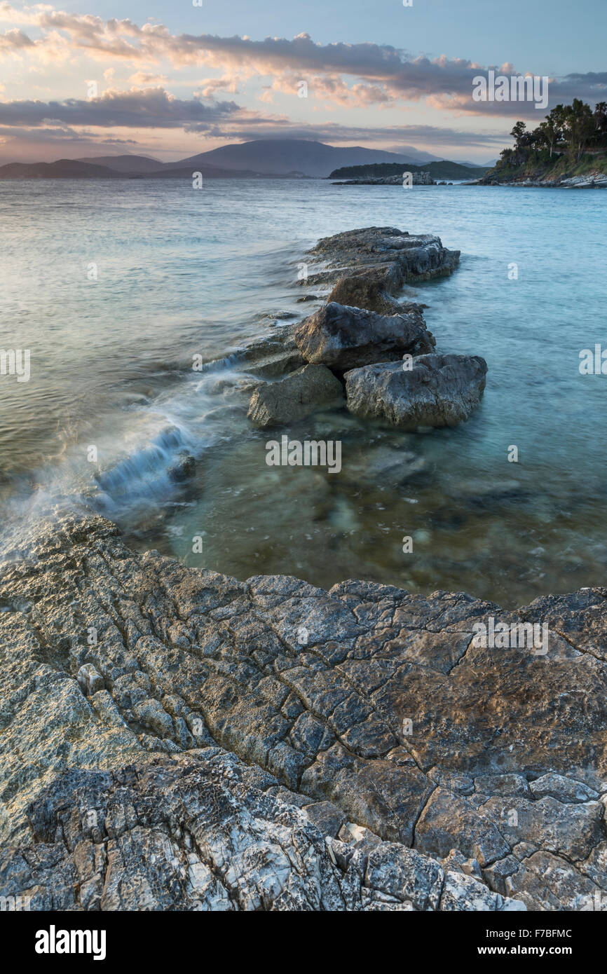 Les rochers sur la plage Kanoni, Kassiopi, Corfou sont éclairés avec la lumière orange du lever du soleil. Banque D'Images