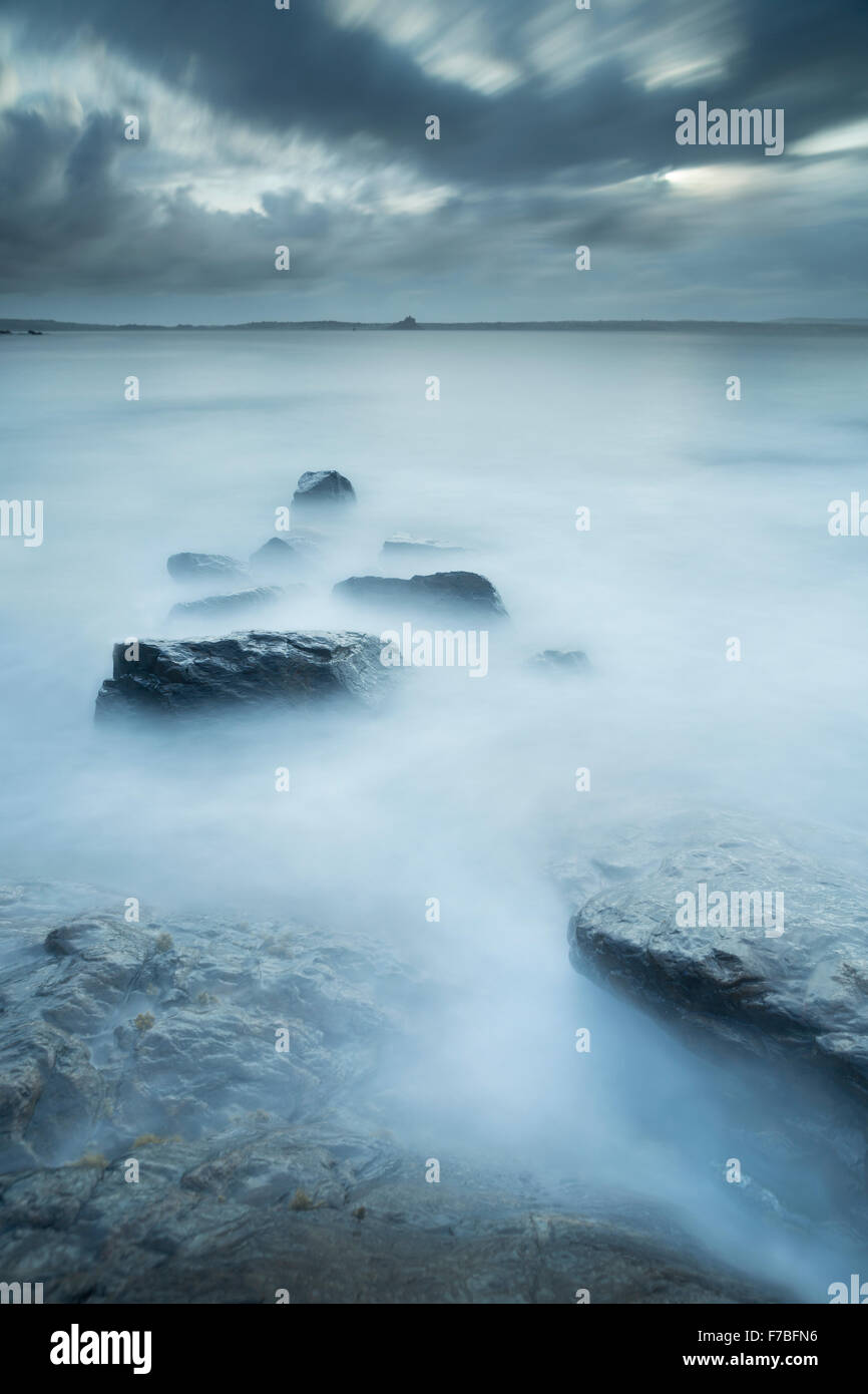 Les vagues sur les rochers sortant de la mer bleue à Mousehole, Cornwall. Saint Michael's Mount peut être vu dans la distance Banque D'Images