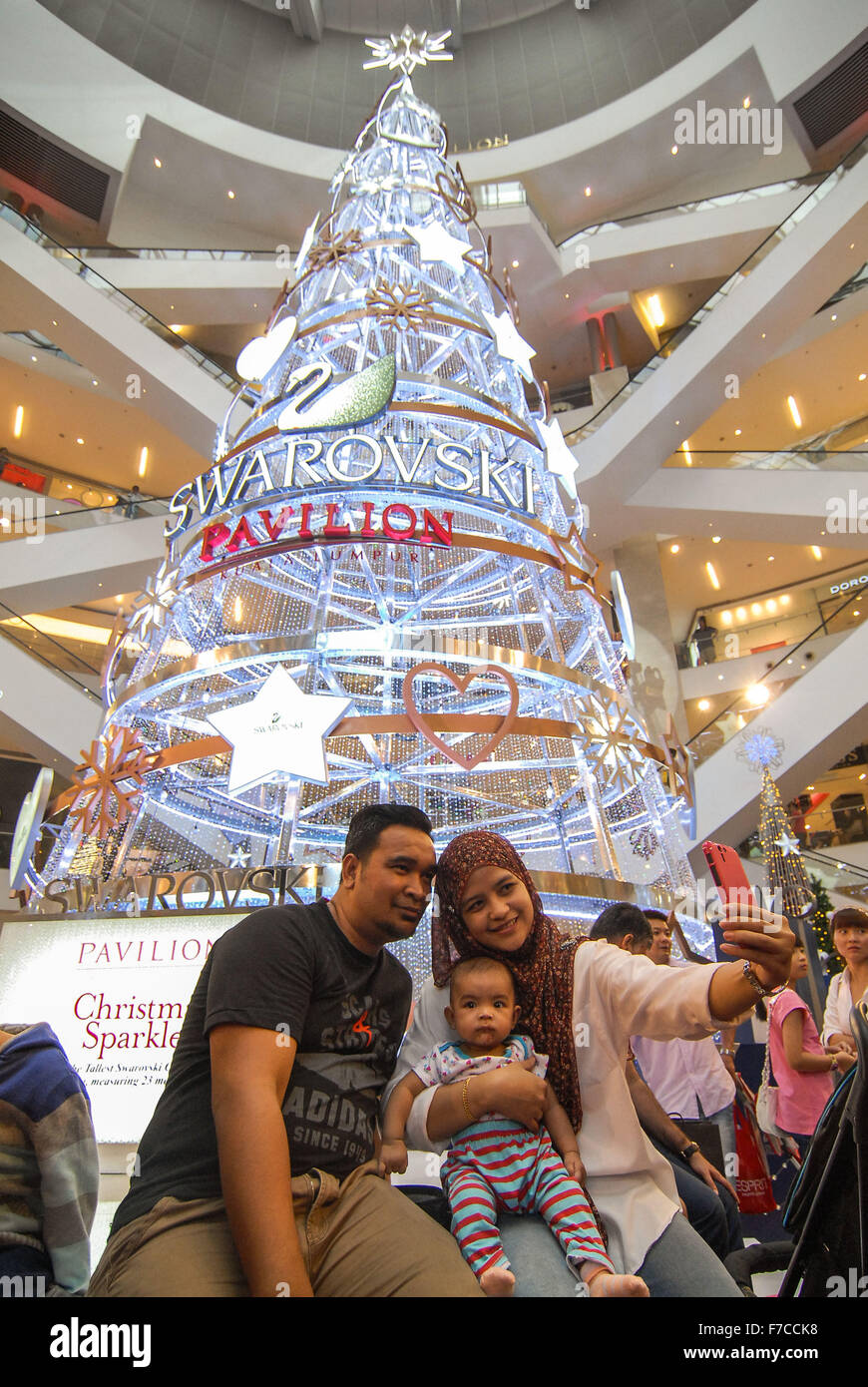 Kuala Lumpur, Malaisie. 29 Nov, 2015. Un couple prend des photos avec leur enfant à côté de l'arbre de Noël de cristal à un centre commercial à Kuala Lumpur, Malaisie, le 29 novembre 2015. Les 23 mètres de haut a été faite de l'arbre de Noël de 170 000 morceaux de crystal par Swarovski pour fêter Noël cette année. © Chong Chung Voon/Xinhua/Alamy Live News Banque D'Images