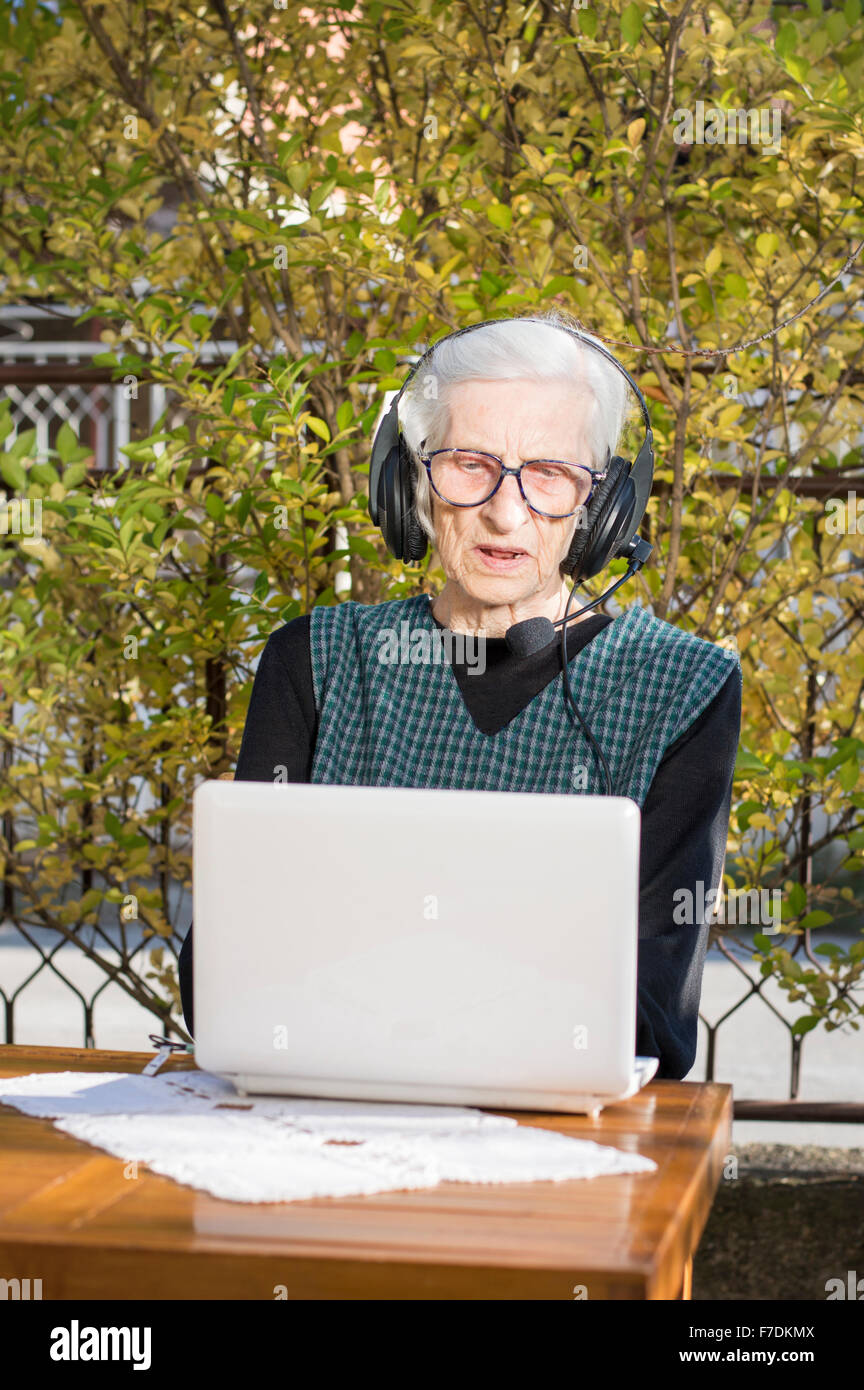 Senior woman having un appel vidéo sur un ordinateur portable dans l'arrière-cour de l'utilisation des écouteurs Banque D'Images Senior woman having un appel vidéo sur un ordinateur portable dans l'arrière-cour de l'utilisation des écouteurs Banque D'Images