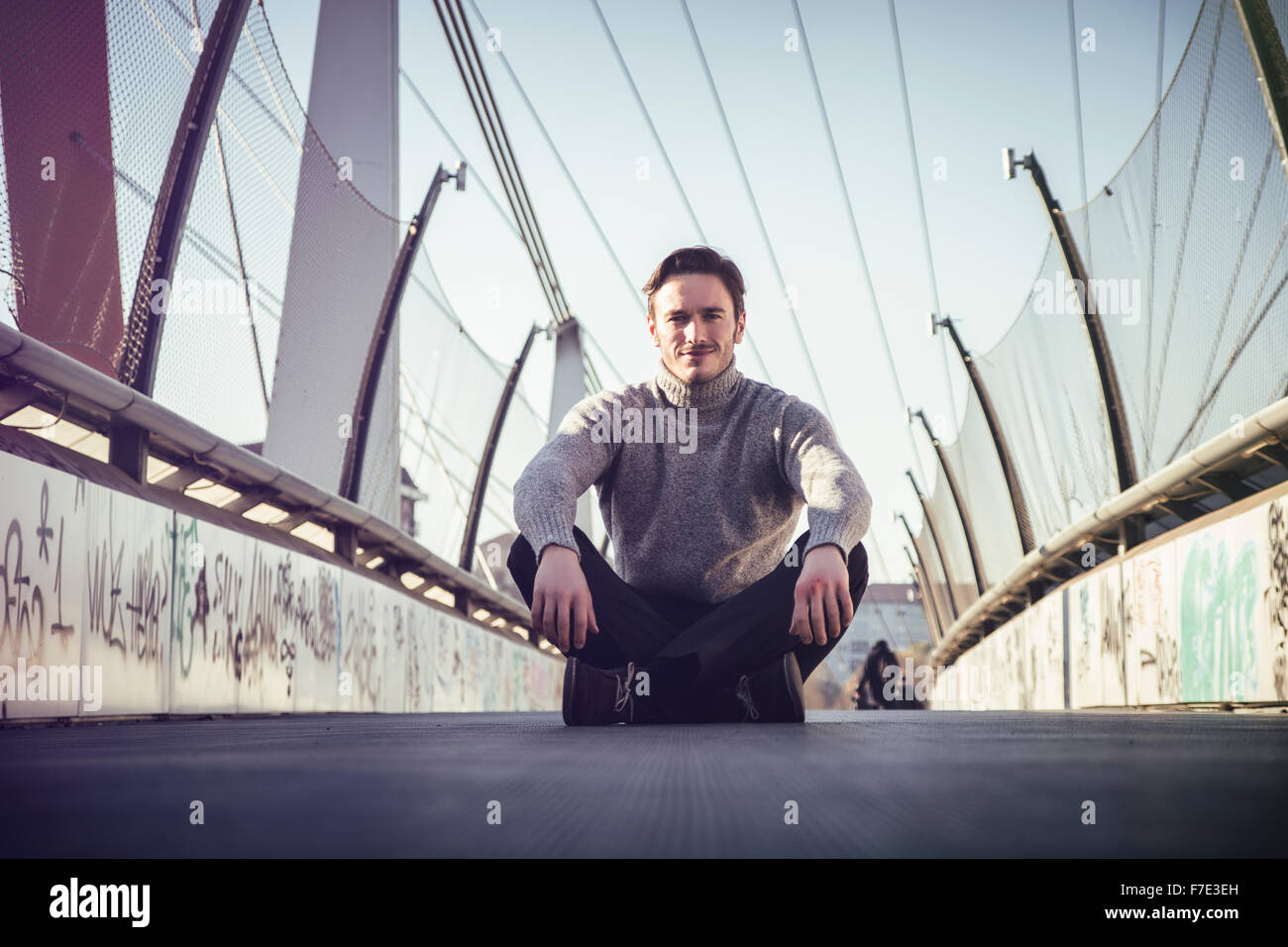 Beau jeune homme assis à l'extérieur dans l'environnement urbain, portant des vêtements d'hiver Banque D'Images