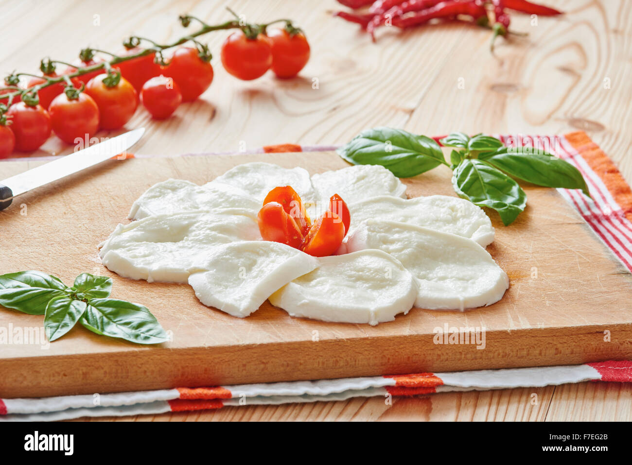 Tranches de mozzarella sur une planche à découper entouré par la tomate et basilic sur une table en bois Banque D'Images