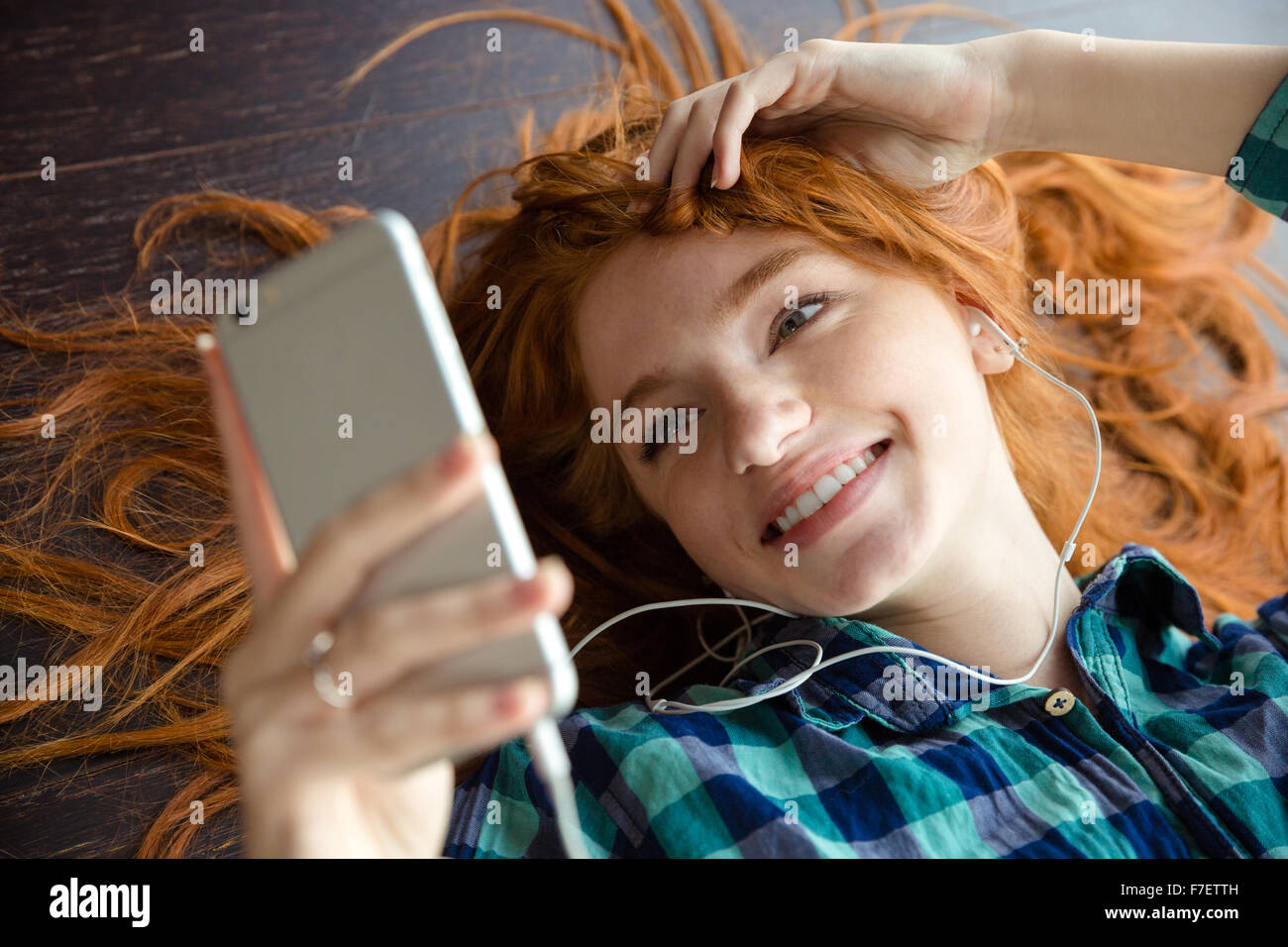 Jeune femme rousse positive joyeuse chemise à carreaux à l'écoute de musique et souriant Banque D'Images