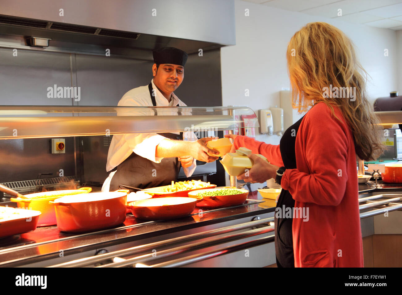 Un membre du personnel de cantine le transfert d'un client de la nourriture dans des contenants à emporter dans une cantine bureau moderne Banque D'Images