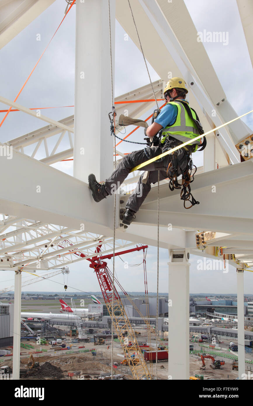Un travailleur de la construction utilise des cordes pour toit d'acier pour l'accès de la construction du nouveau terminal 2 d'Heathrow à Londres. Banque D'Images