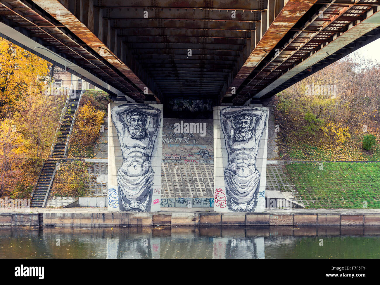 Graffiti créatif sous un pont au-dessus de la rivière Neris, à Vilnius, Lituanie. deux statues atlant peint "holding" un pont Banque D'Images