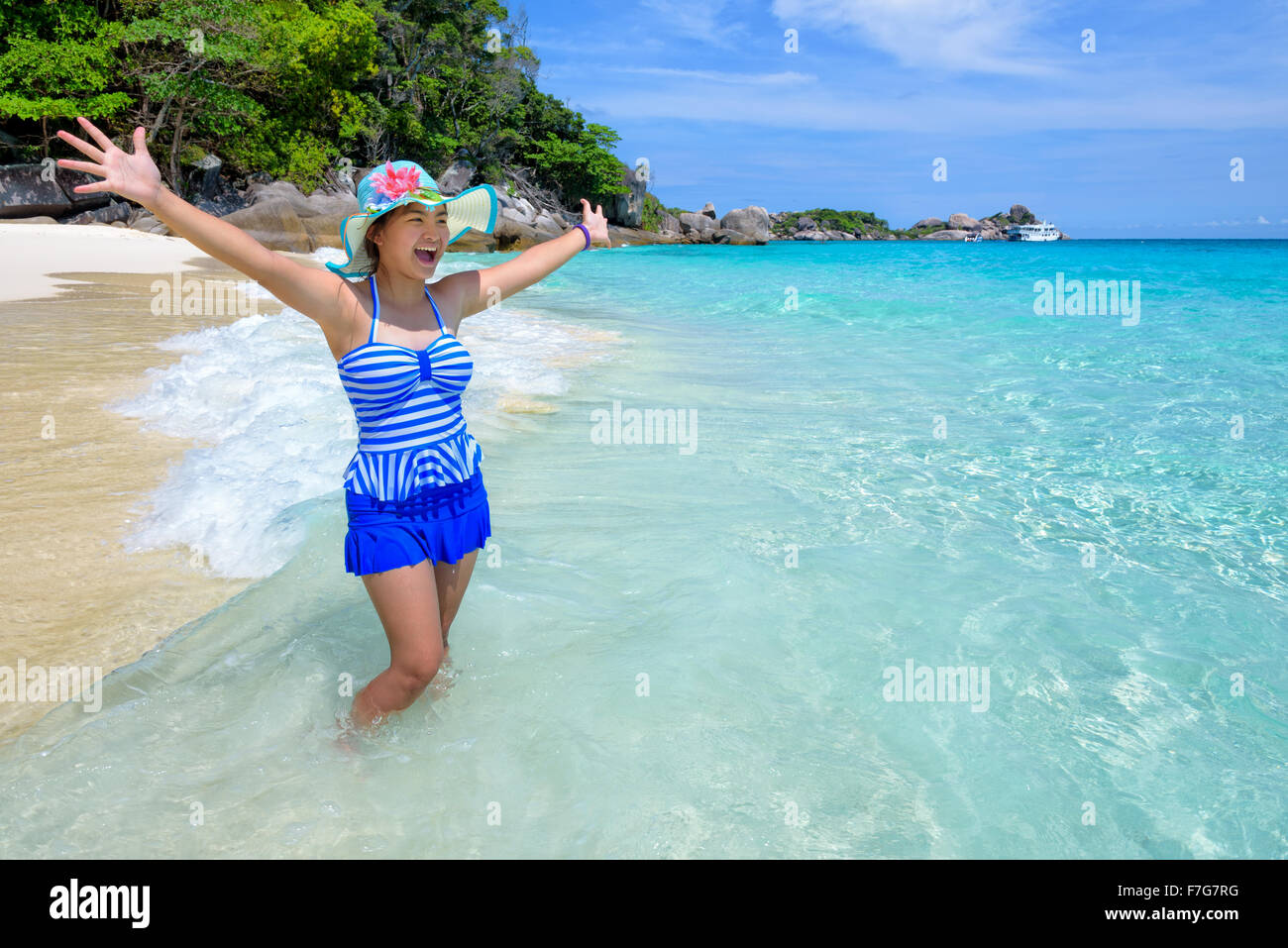 Belle femme dans un maillot de bain bleu à rayures hat standing with arms outstretched à la vie insouciante au ciel et mer en été Banque D'Images