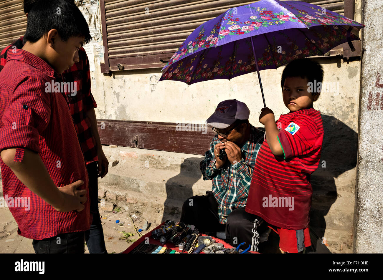 Un enfant portant le Portugal football jersey couvre père au travail avec un parapluie de couleur pourpre, Katmandou, Népal, 2015 Banque D'Images