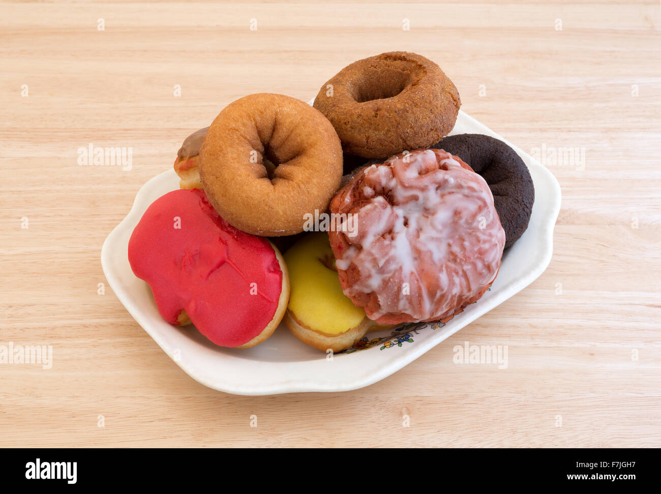 Un vieux plateau avec plusieurs donuts et d'un beignet de cerise glacé au sommet d'une table en bois éclairé par la lumière naturelle. Banque D'Images