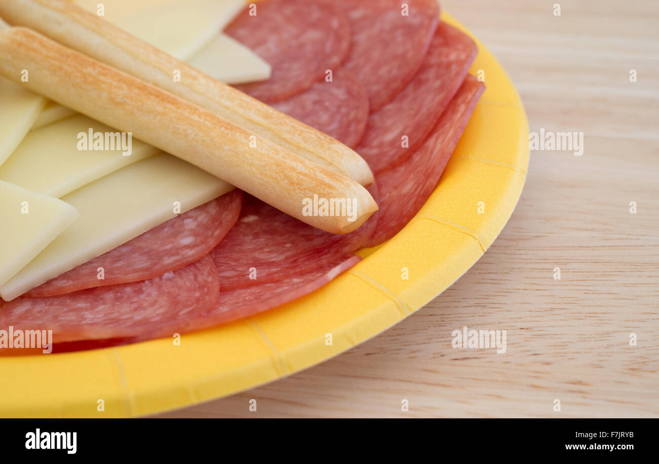 Une plaque de papier jaune avec des tranches de salami de Gênes et de fromage provolone gressins plus sur une table en bois Banque D'Images