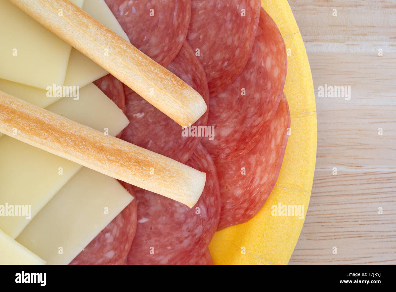 Haut de page fermer d'un papier jaune plaque avec des tranches de salami de Gênes et de fromage provolone gressins plus sur une table en bois Banque D'Images