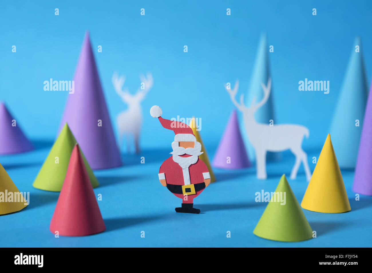 Scène de Noël : coupe papier fait main santa avec cerfs et des formes sur fond bleu. Idéal pour les cartes de vœux de Noël Banque D'Images