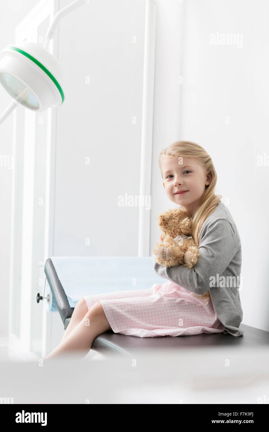 Portrait of smiling girl hugging teddy bear patient in examination room Banque D'Images