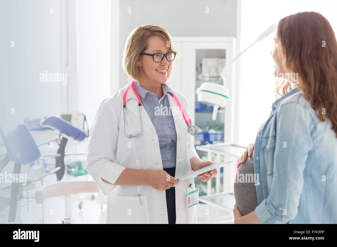 Médecin avec tablette numérique de parler à la patiente enceinte dans la salle d'examen Banque D'Images